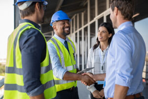 Restoration contractors wearing hard hats and yellow vests shake hands with homeowners