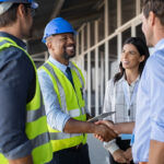 Restoration contractors wearing hard hats and yellow vests shake hands with homeowners