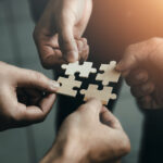 Team members hold puzzle pieces together, representing how building a strong company culture can promote restoration claims success