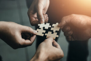 Team members hold puzzle pieces together, representing how building a strong company culture can promote restoration claims success
